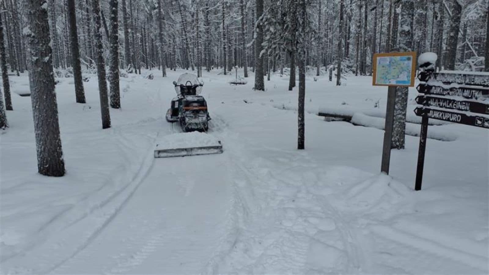 Image: Tapani Seppänen Kuvan keskellä moottorikelkka jonka ympärillä puita. Kuvan alaosassa lunta ja yläosassa metsää. Kuvan oikeassa reunassa viittoja.
