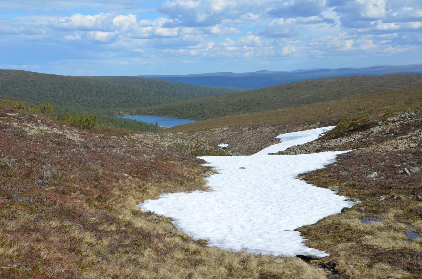 Image: Pasi Nivasalo There is snow in the hollow of the fell. In the background, a lake can be seen.