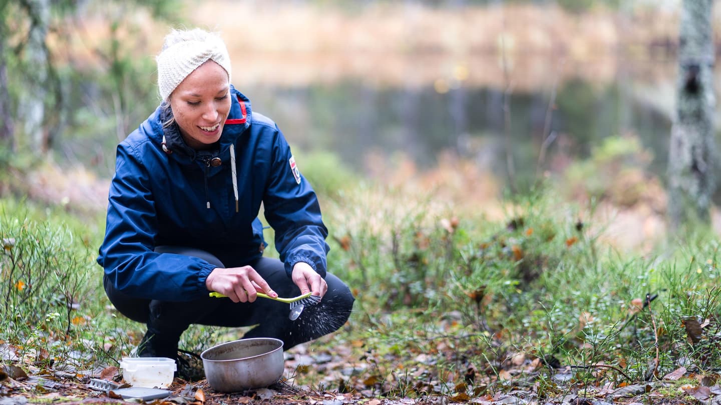 Image: Mitja Piipponen A person is squatting while cleaning cooking utensils well away from the water.