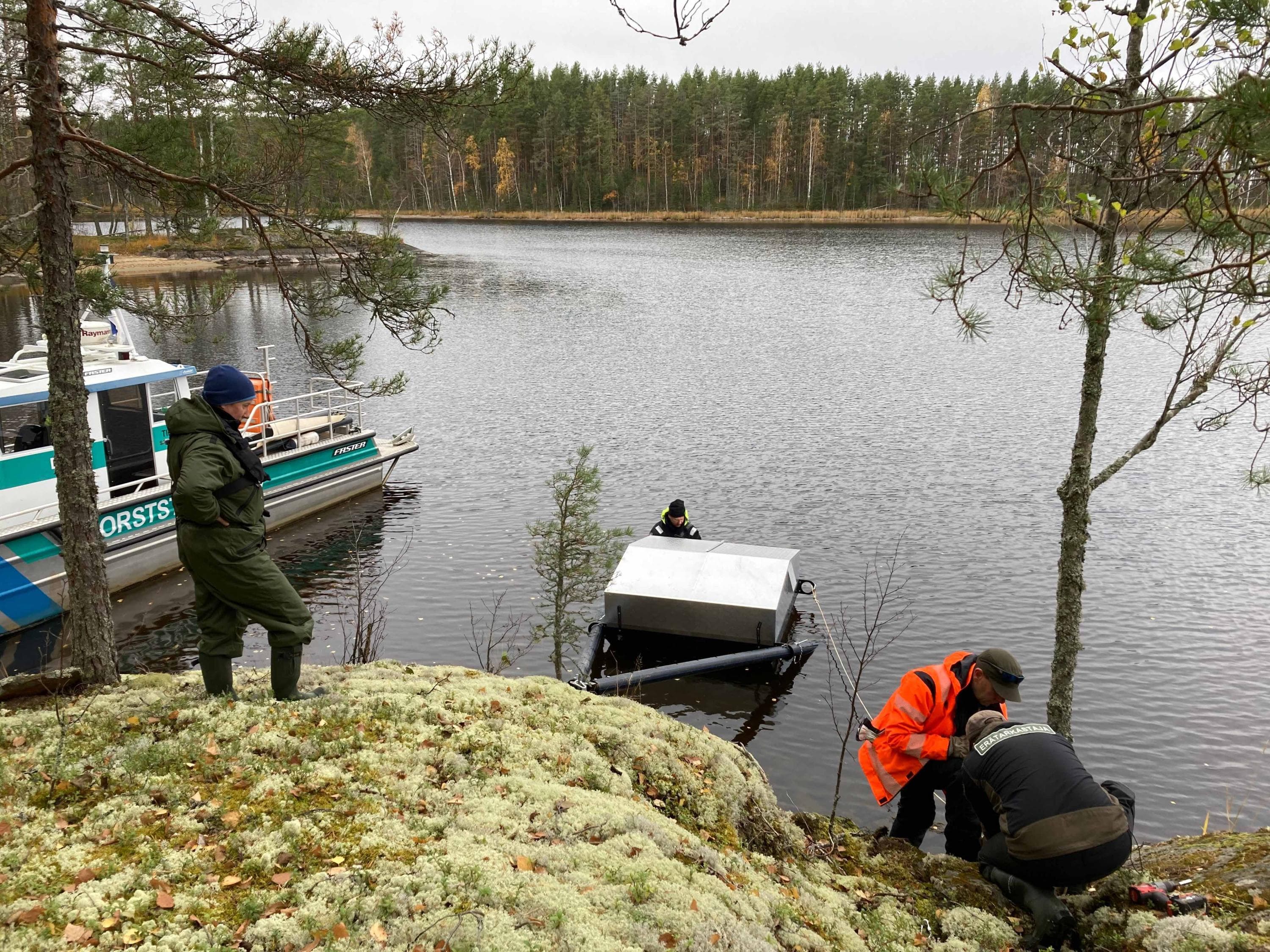 Kuva: Riikka Alakoski Neljä henkilöä asentamassa keinopesää saaren rantaan.