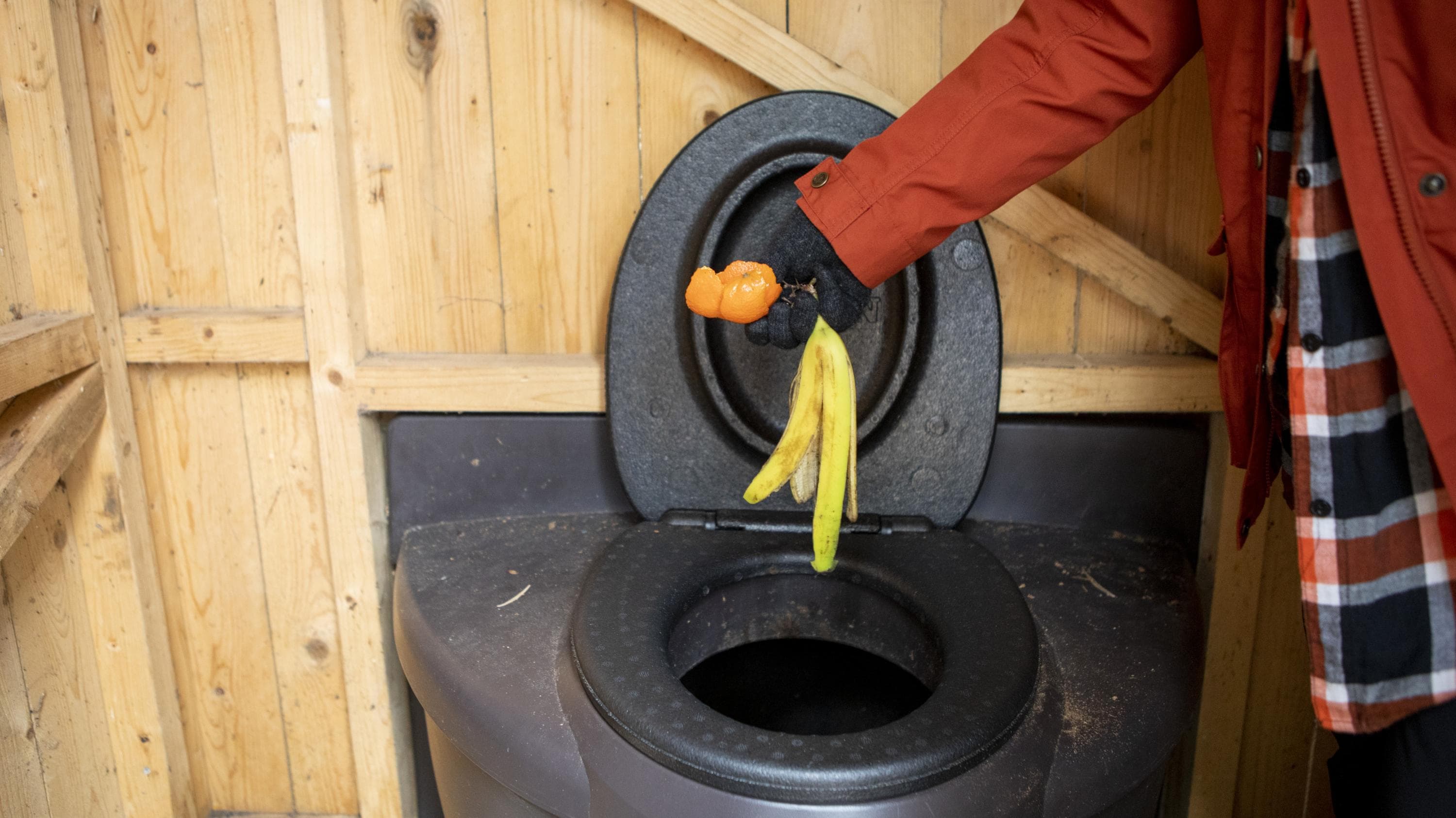 Kuva: Saara Tuominen Henkilö on pudottamassa banaanin ja mandariinin kuoria kompostoivaan käymälään.