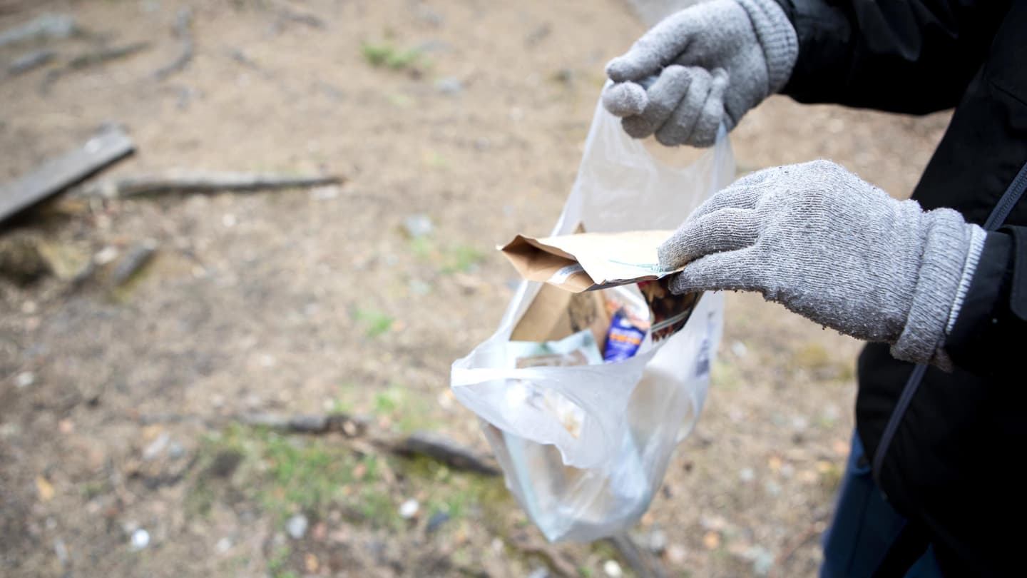 Image: Saara Tuominen A person is outdoors in nature, putting litter into a small fruit bag.