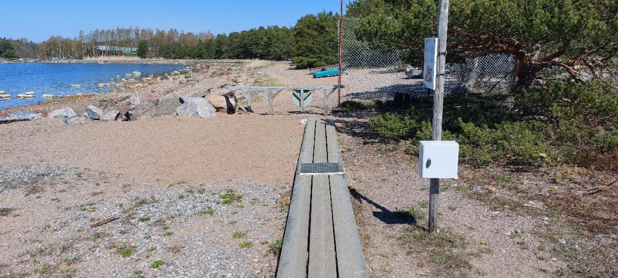 Image: Metsähallitus A boardwalk along a summer shoreline, with an information sign and a box on a post beside it.