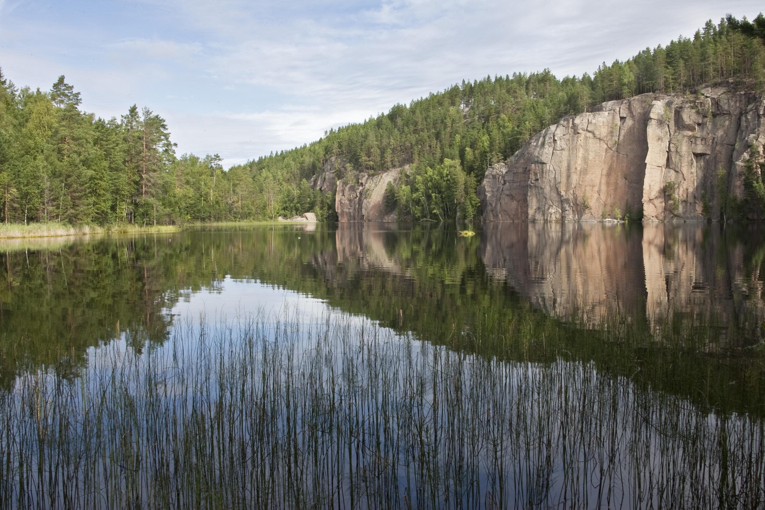 Kuva: Lassi Kujala Tyyni lampi, jonka takana kohoaa äkkijyrkkä kallio.