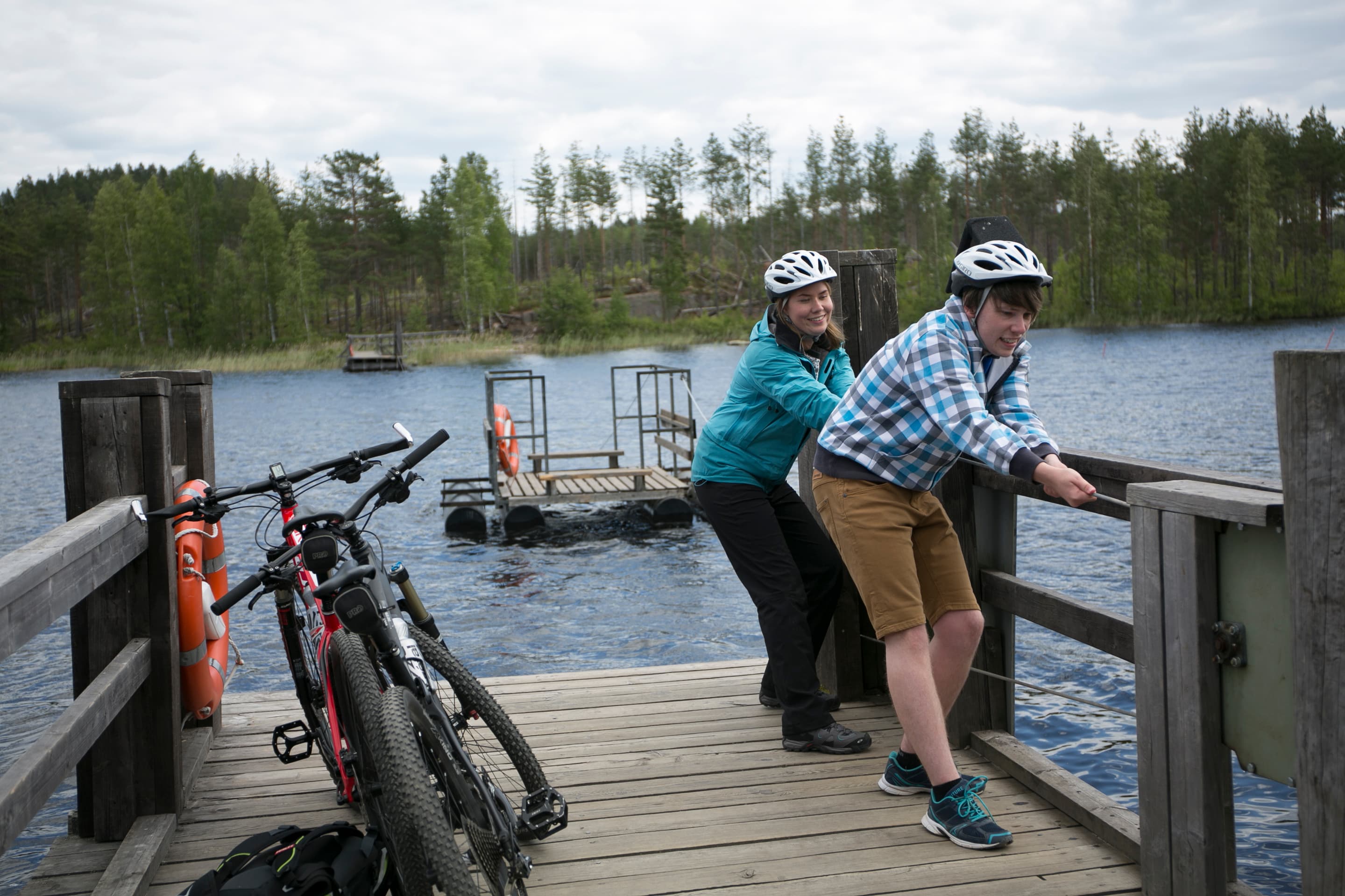 Kuva: Saara Lavi Kaksi pyöräilijää laiturilla. He vetävät köydestä lossia lähemmäksi laituria.