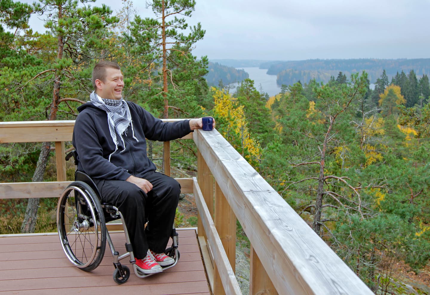 Image: Tuomas Uola A visitor using a wheelchair stands by the railing of an accessible viewing platform, looking out over the autumn landscape.