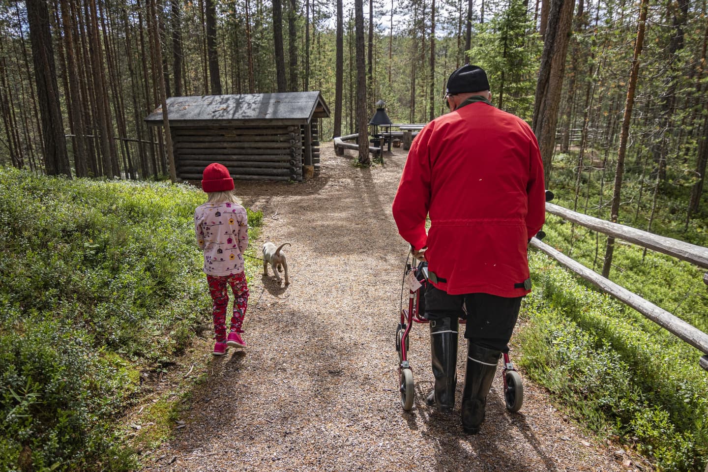 Kuva: Jonna Kalliomäki Etualalla vaeltaja rollaattorin kanssa sekä lapsi ja koira kävelemässä kamerasta pois päin. Taustalla näkyy esteetön reitti, tulipaikka ja metsää.