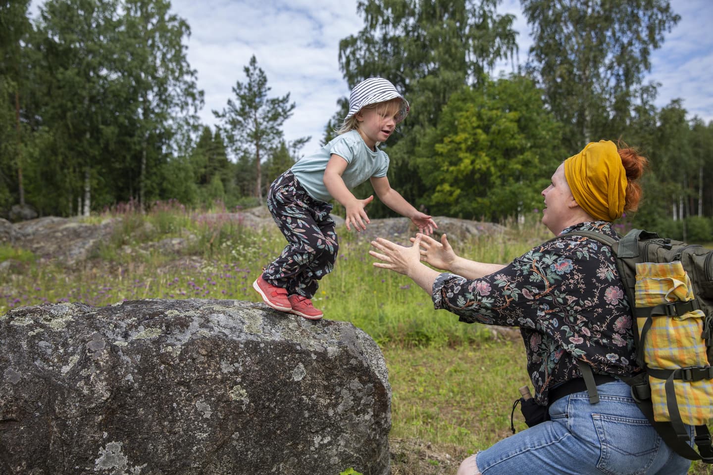 Kuva: Saara Lavi Lapsi on hyppäämässä korkean kiven päältä aikuisen syliin niityllä Linnansaaren kansallispuistossa.