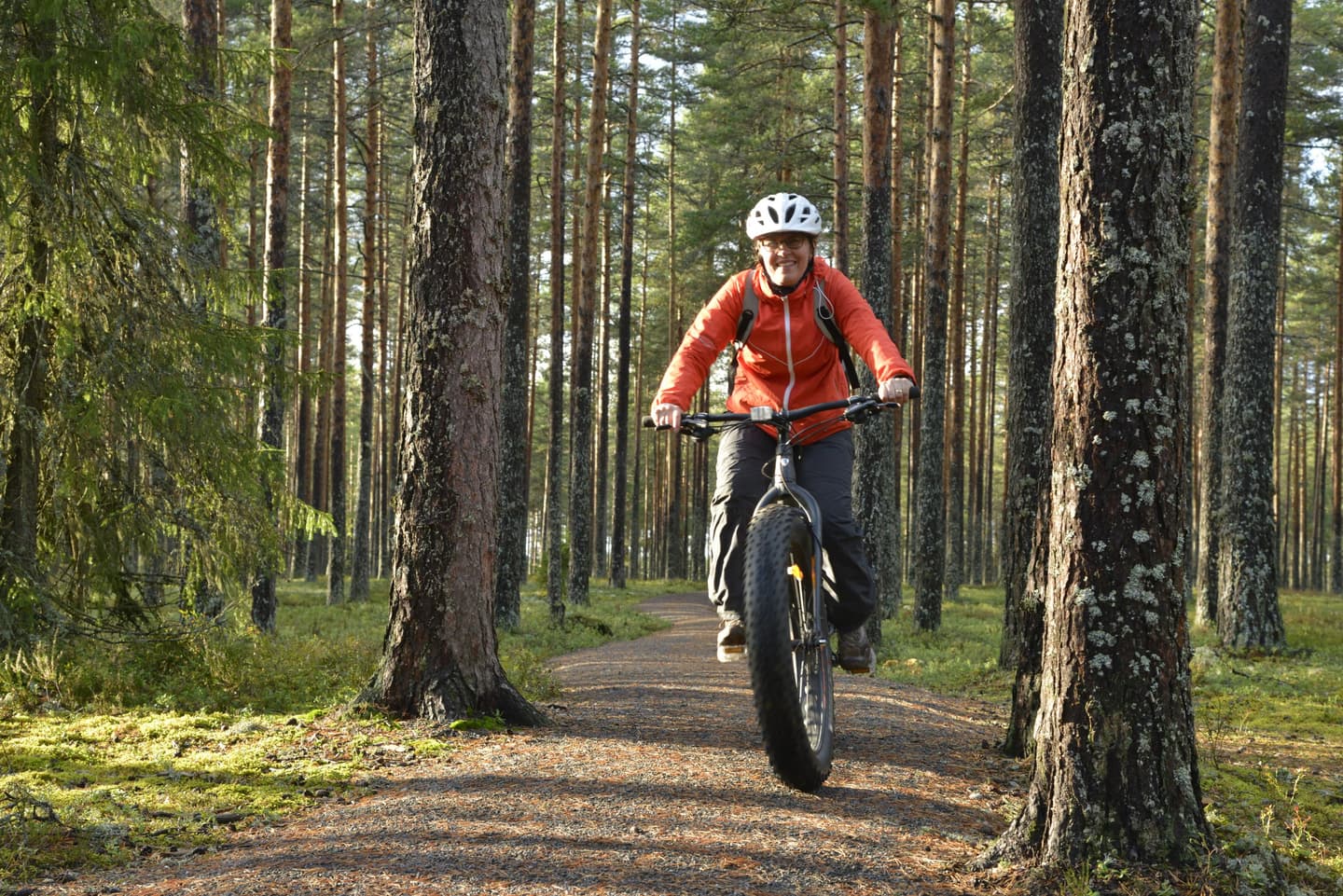 Kuva: Terttu Hermansson Hymyilevä maastopyöräilijä leveällä polulla. Taustalla syksyistä metsää.