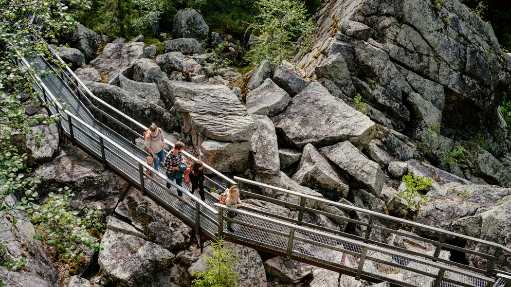 Två personer och tre barn går på en metallstrukturerad stig omgiven av ett stenigt landskap.