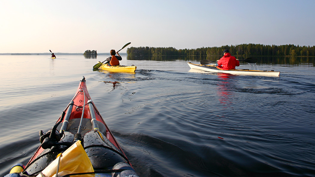 Neljä kajakkimelojaa tyynellä järvellä melomassa kohti järven selkää. Unelmatyyni melontakeli Simojärvellä. Kuva: Olli Vainio