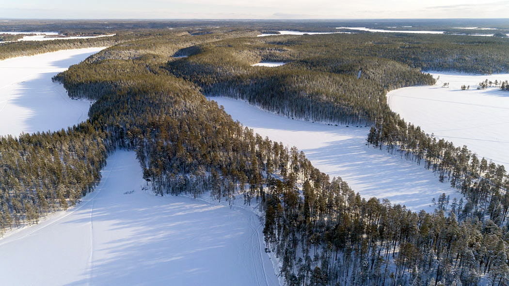 Ett flygfotografi av en mosaik av vattendrag och skogar. Spår kan ses på de snötäckta sjöarna.