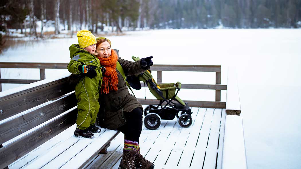 Ett barn och en vuxen sitter på bänken vid en frusen sjö.