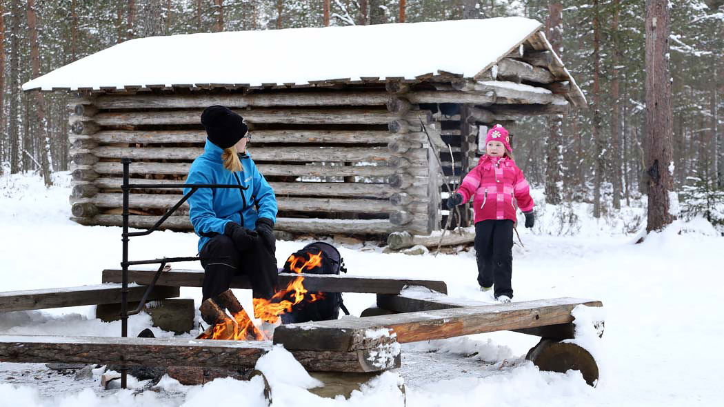 Aikuinen ja lapsi viettävät aikaa nuotiolla talvisessa metsässä.
