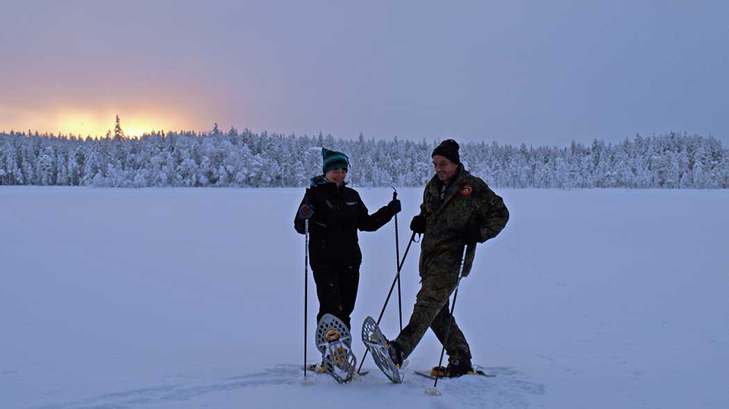 Kaksi lumikenkäilijää kaamoksen hämyssä järven jäällä.