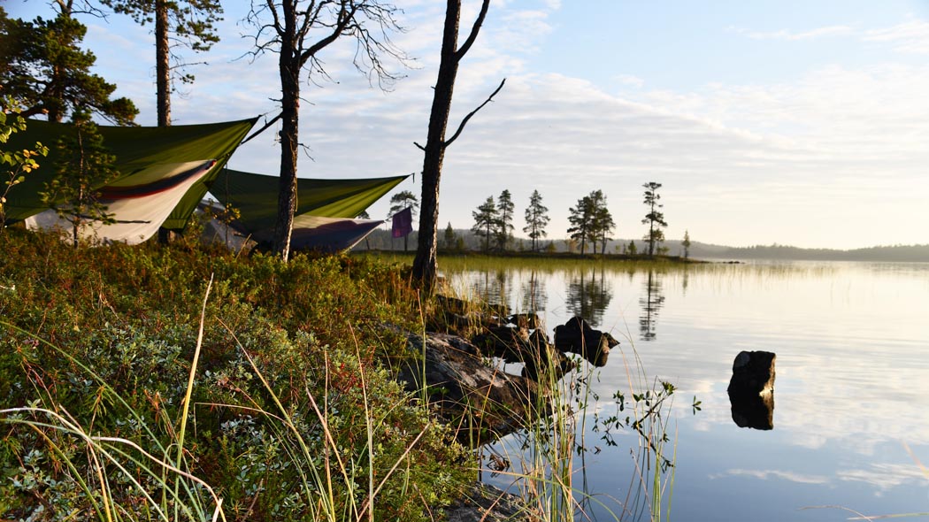 Ilta-auringossa järven rannalla viritetty puihin riippumattoja yöpymistä varten.