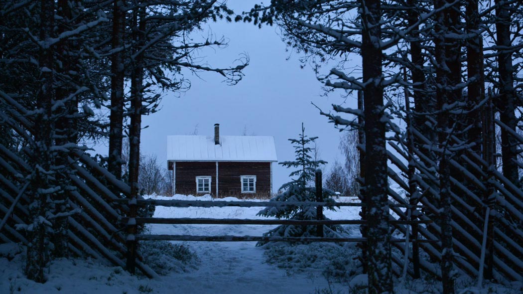 Talvisessa kuvassa on vanhaa riukuaitaa ja tilan päärakennus. Maassa ja puissa on lunta.