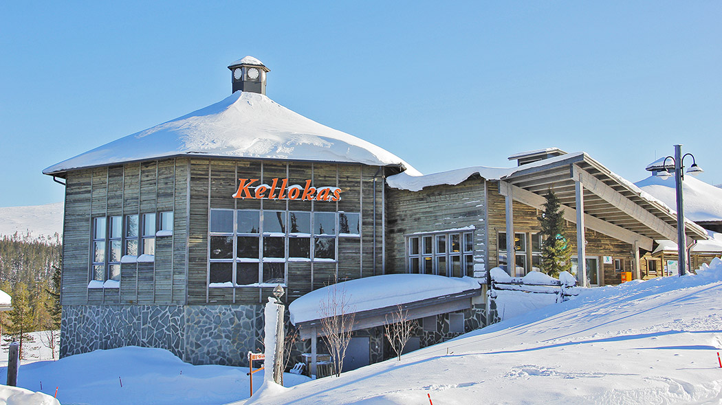 Talvisessa kuvassa iso moderni rakennus, jonka seinässä lukee nimi Kellokas. Rakennus on rinteessä. Taustalla luminen tunturi. On aurinkoinen talvipäivä.