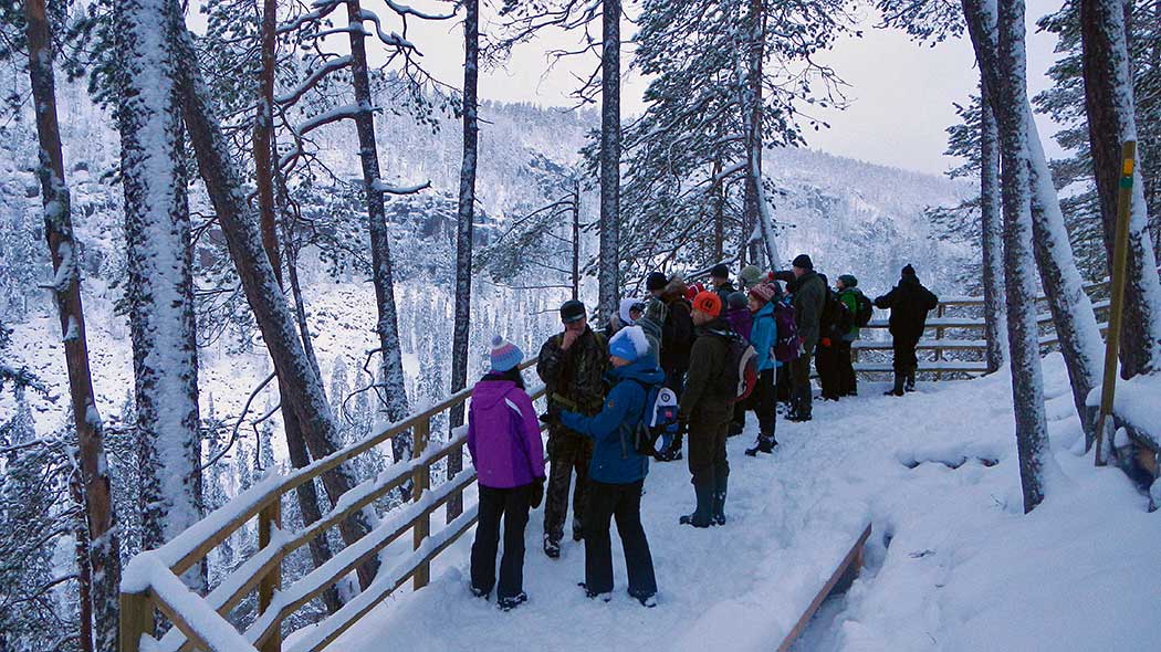 Folk står vid en utsiktsplats med ett räcke på vintern. I bakgrunden finns en bred kanjondal.